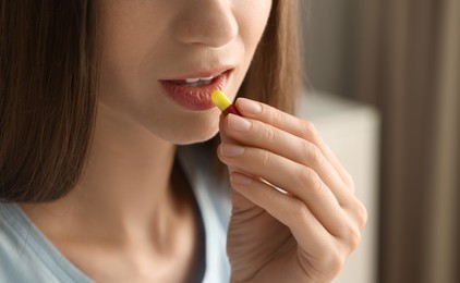 Woman taking pill on blurred background, closeup