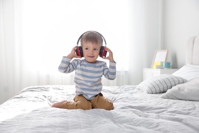 Cute little baby in headphones on bed at home