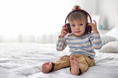 Photo of Cute little baby in headphones on bed at home, space for text