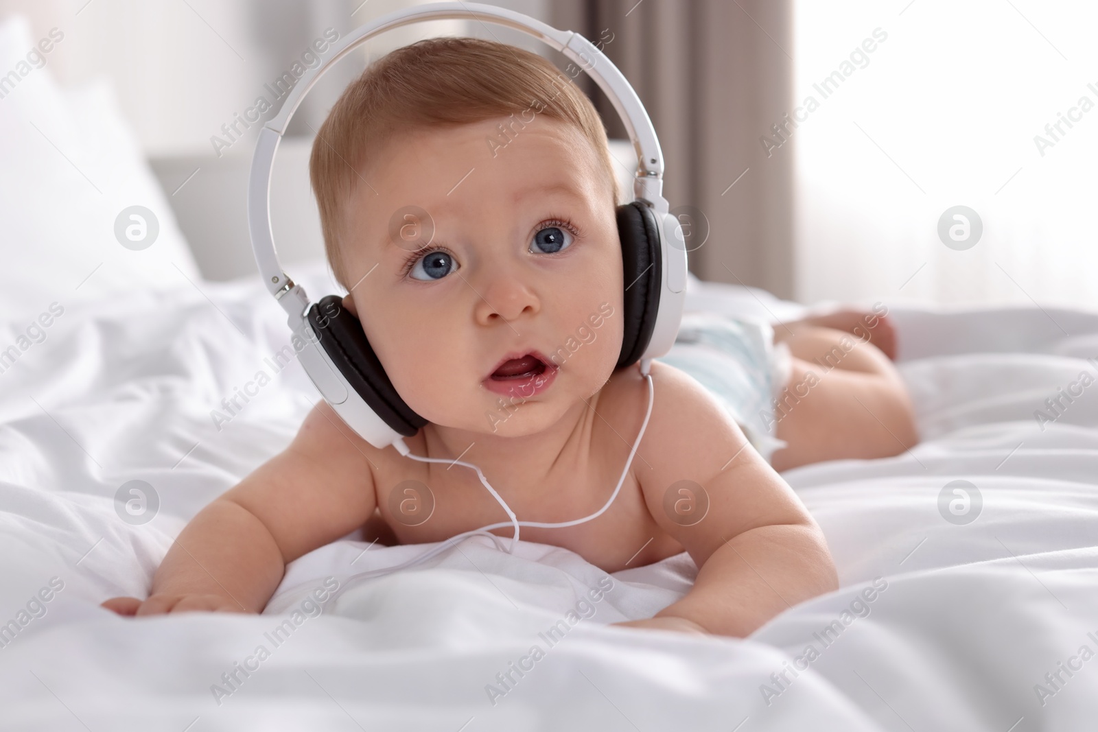 Photo of Cute little baby with headphones on bed at home