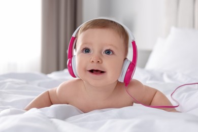 Cute little baby with headphones on bed at home