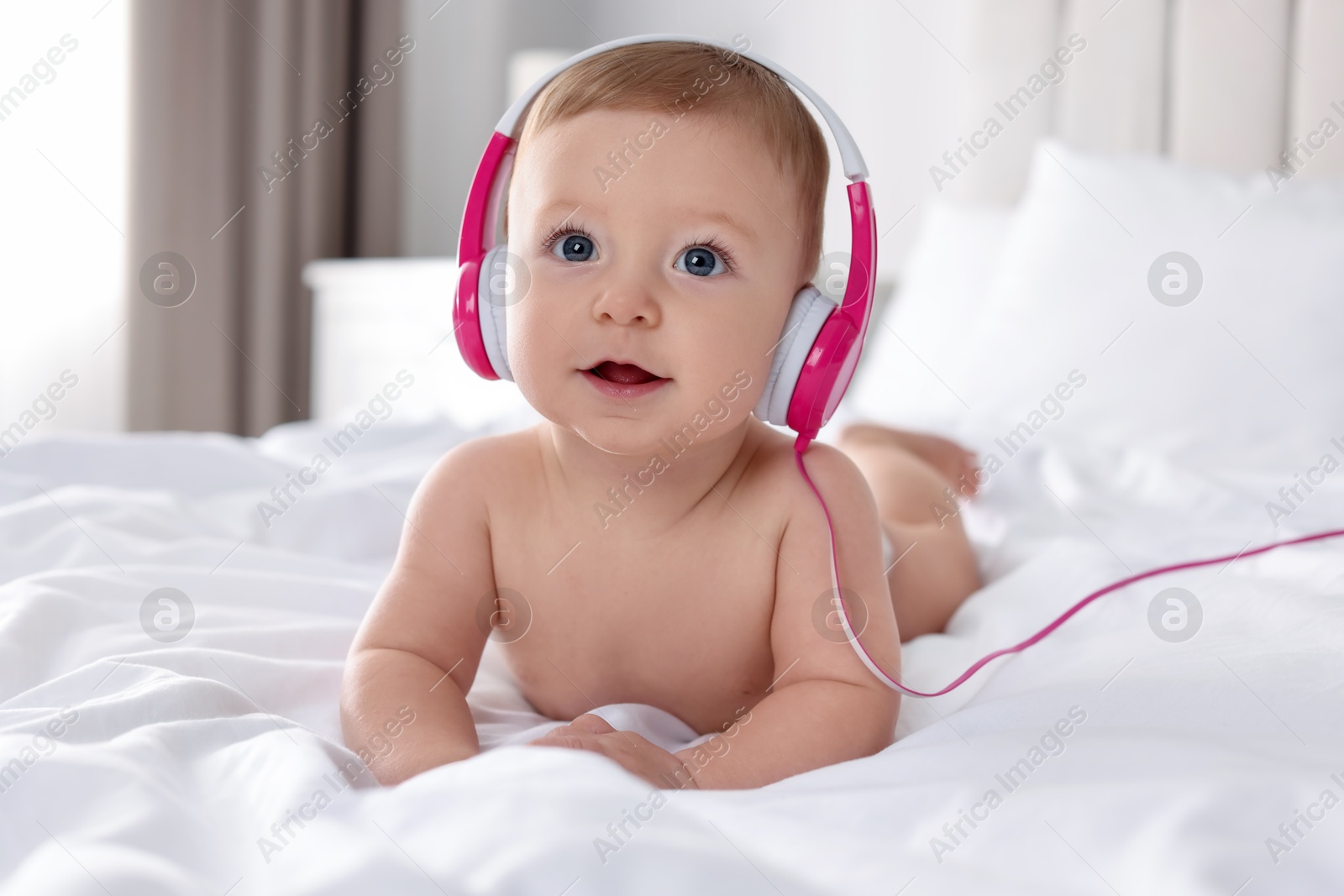 Photo of Cute little baby with headphones on bed at home