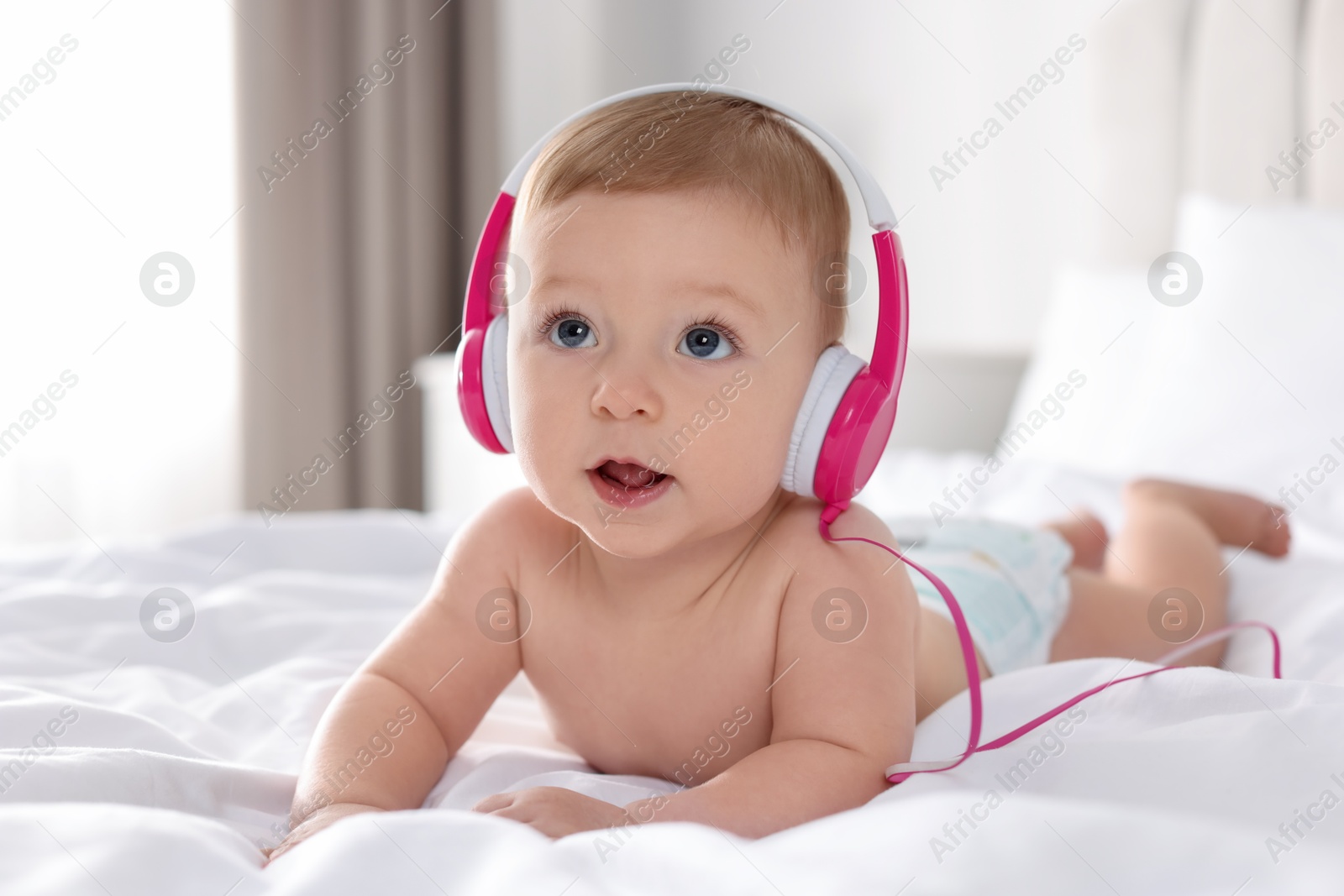 Photo of Cute little baby with headphones on bed at home