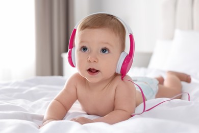 Photo of Cute little baby with headphones on bed at home