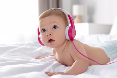 Photo of Cute little baby with headphones on bed at home