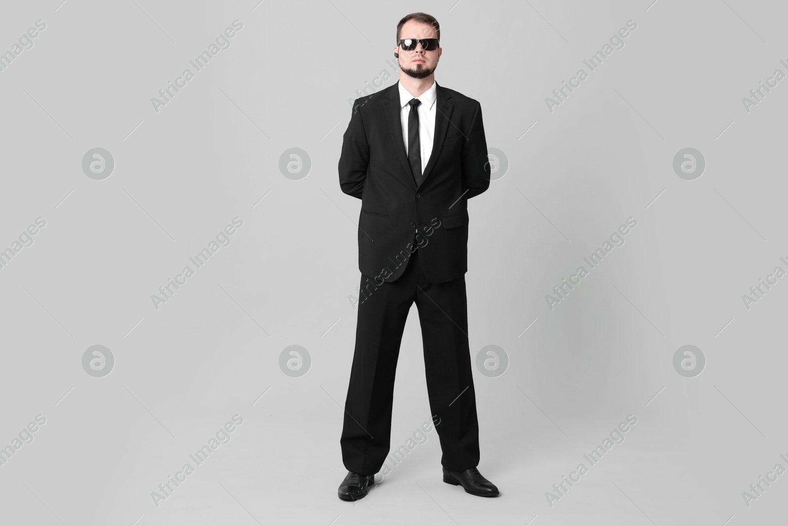 Photo of Young bodyguard in suit and sunglasses on grey background