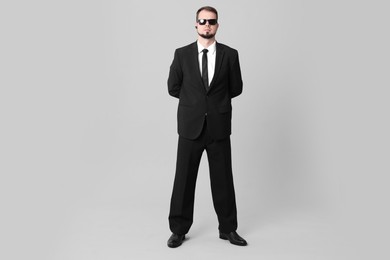 Young bodyguard in suit and sunglasses on grey background