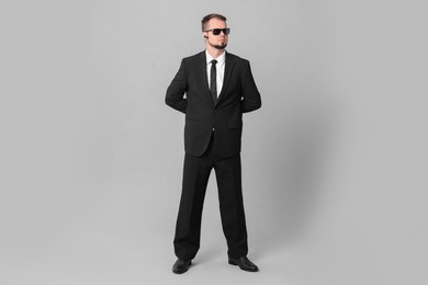 Young bodyguard in suit and sunglasses on grey background