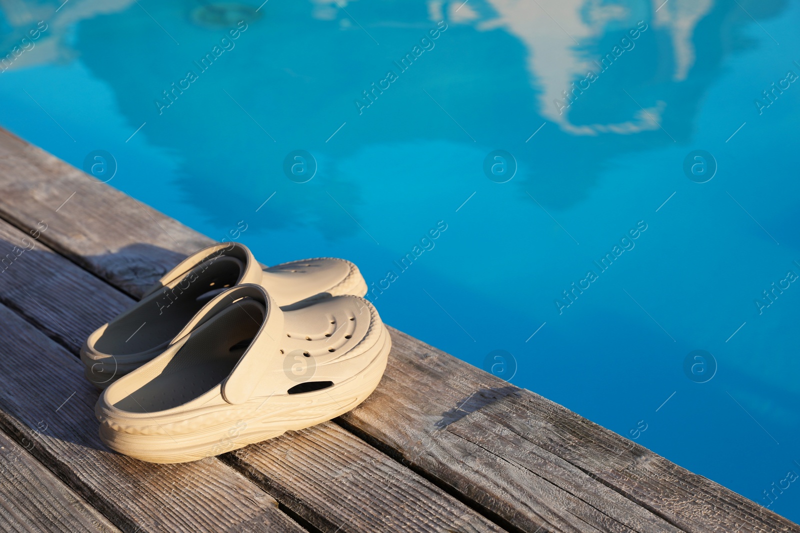 Photo of Stylish beach slippers on wooden deck near outdoor swimming pool