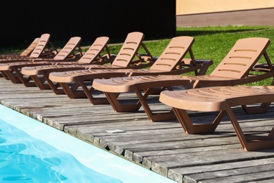 Photo of Empty sun loungers on wooden deck near outdoor swimming pool