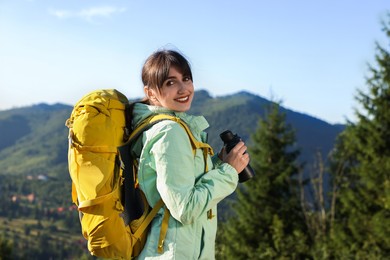 Smiling woman with backpack and binoculars in beautiful mountains