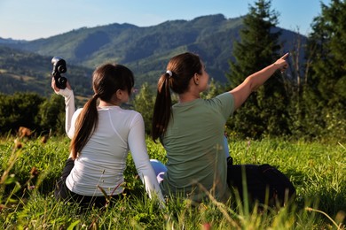 Women with binoculars on green grass in beautiful mountains, back view