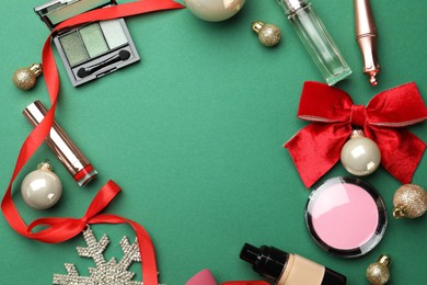 Photo of Frame made of makeup products and Christmas decor on green background, flat lay. Space for text