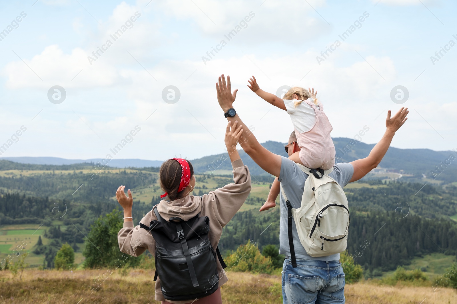 Photo of Family of tourists with backpacks enjoying picturesque landscape with wide open arms, back view