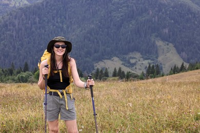 Photo of Young hiker with backpack and trekking poles in mountains, space for text