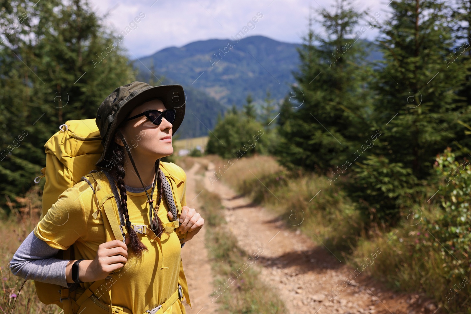 Photo of Young hiker with hat, sunglasses and backpack outdoors, space for text