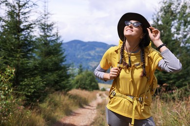 Young hiker with hat, sunglasses and backpack outdoors, space for text