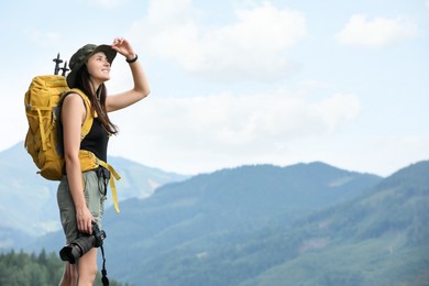 Young hiker with backpack and camera in mountains, space for text