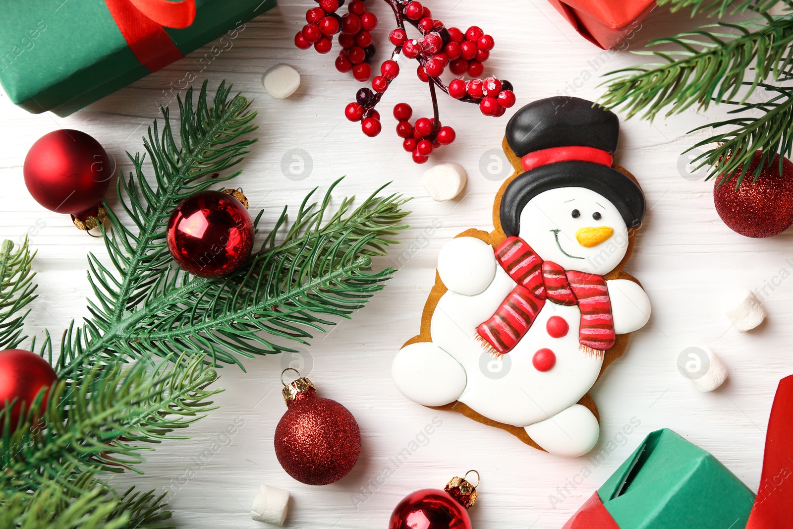 Photo of Delicious cookie in shape of snowman, marshmallows and Christmas decor on white wooden table, flat lay