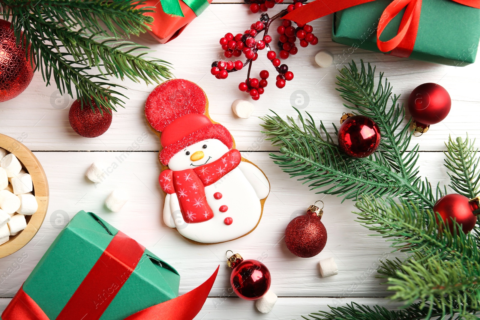 Photo of Delicious cookie in shape of snowman, marshmallows and Christmas decor on white wooden table, flat lay