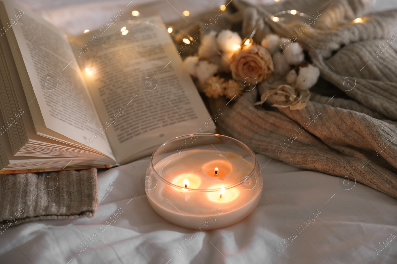 Photo of Burning candle, book, sweater and dry flowers on white cloth. Autumn aesthetics