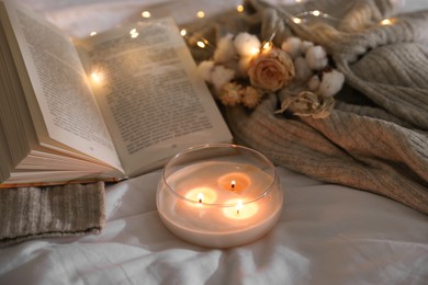 Photo of Burning candle, book, sweater and dry flowers on white cloth. Autumn aesthetics