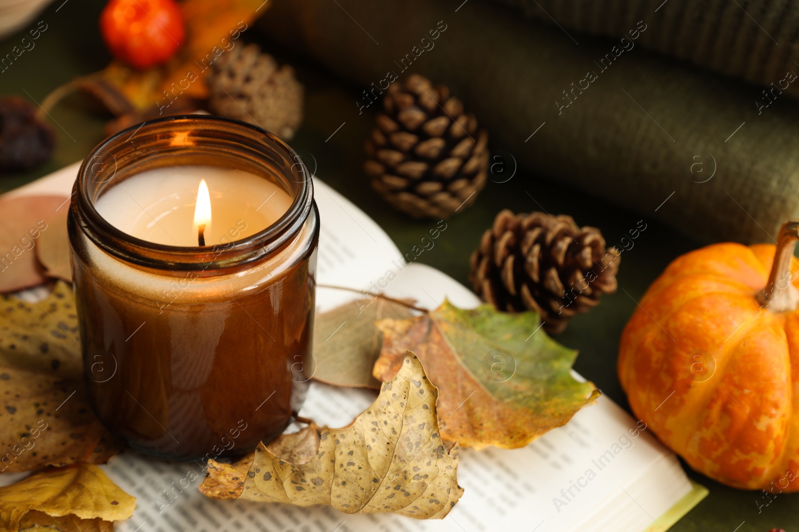 Photo of Burning candle and dry leaves on open book, closeup. Autumn atmosphere