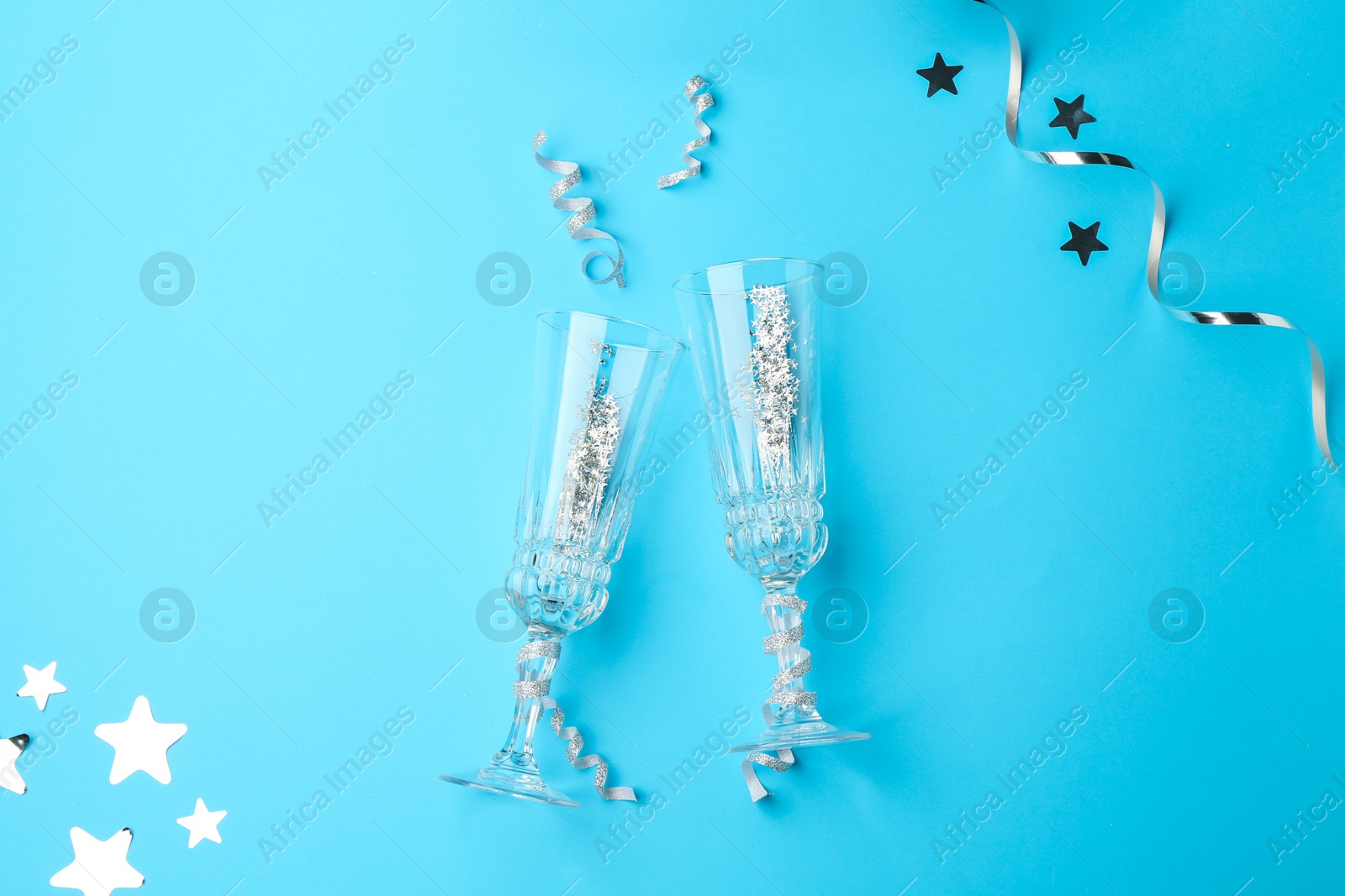 Photo of Confetti and glasses on light blue background, flat lay. Christmas decor