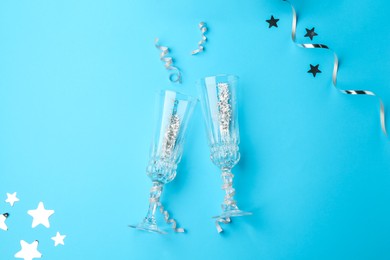 Photo of Confetti and glasses on light blue background, flat lay. Christmas decor