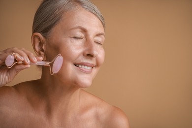 Beautiful woman doing facial massage with roller on beige background, space for text