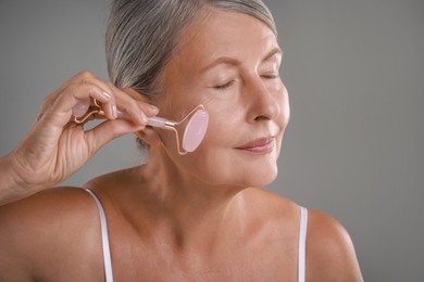 Beautiful woman doing facial massage with roller on grey background