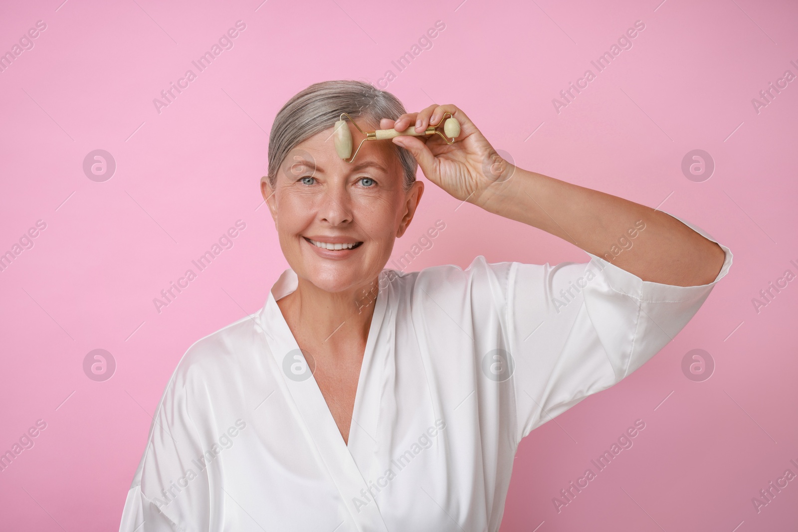 Photo of Beautiful woman doing facial massage with roller on pink background