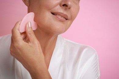 Photo of Woman doing facial massage with gua sha tool on pink background, closeup