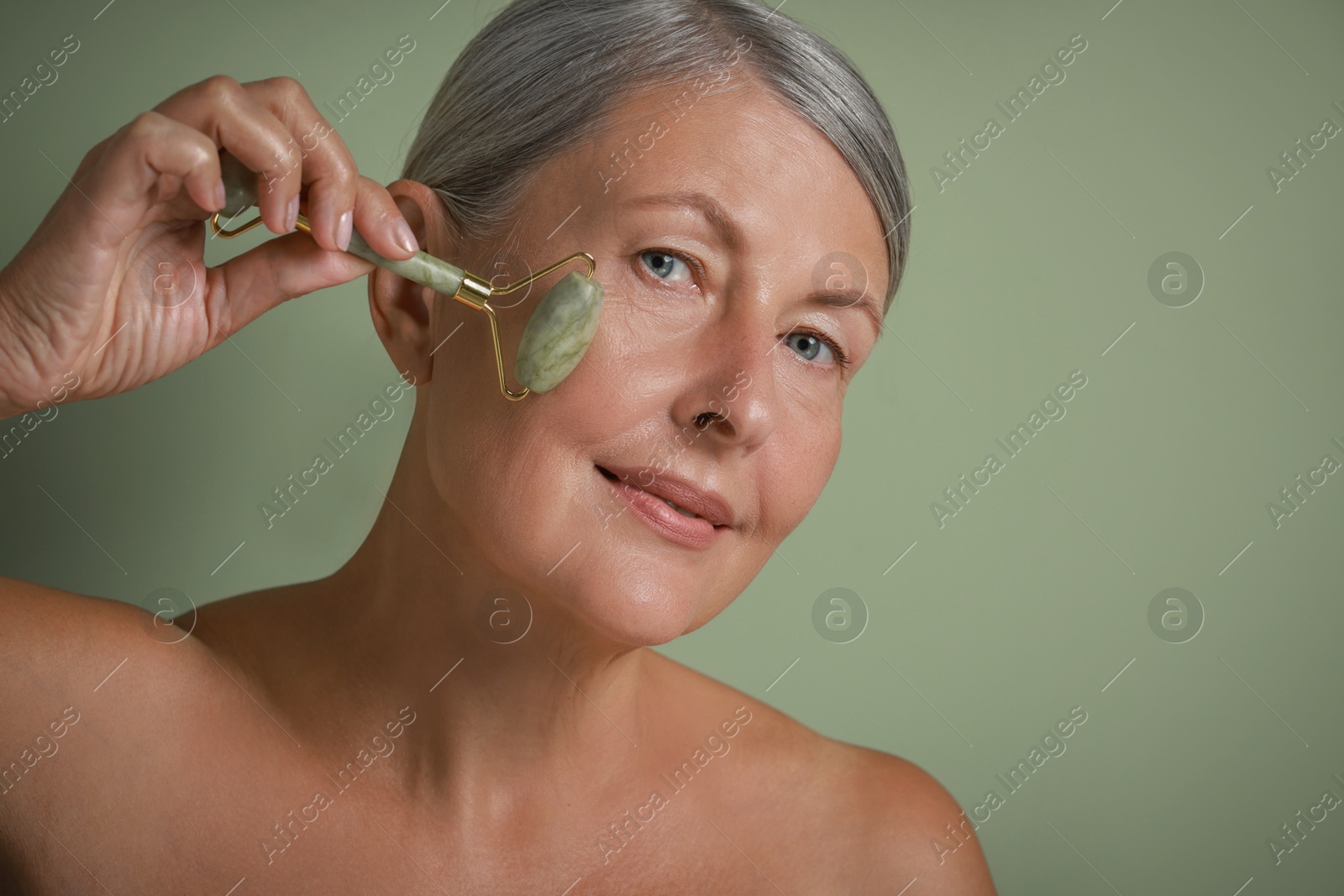 Photo of Beautiful woman doing facial massage with roller on light green background