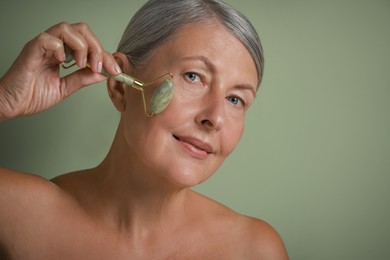 Beautiful woman doing facial massage with roller on light green background