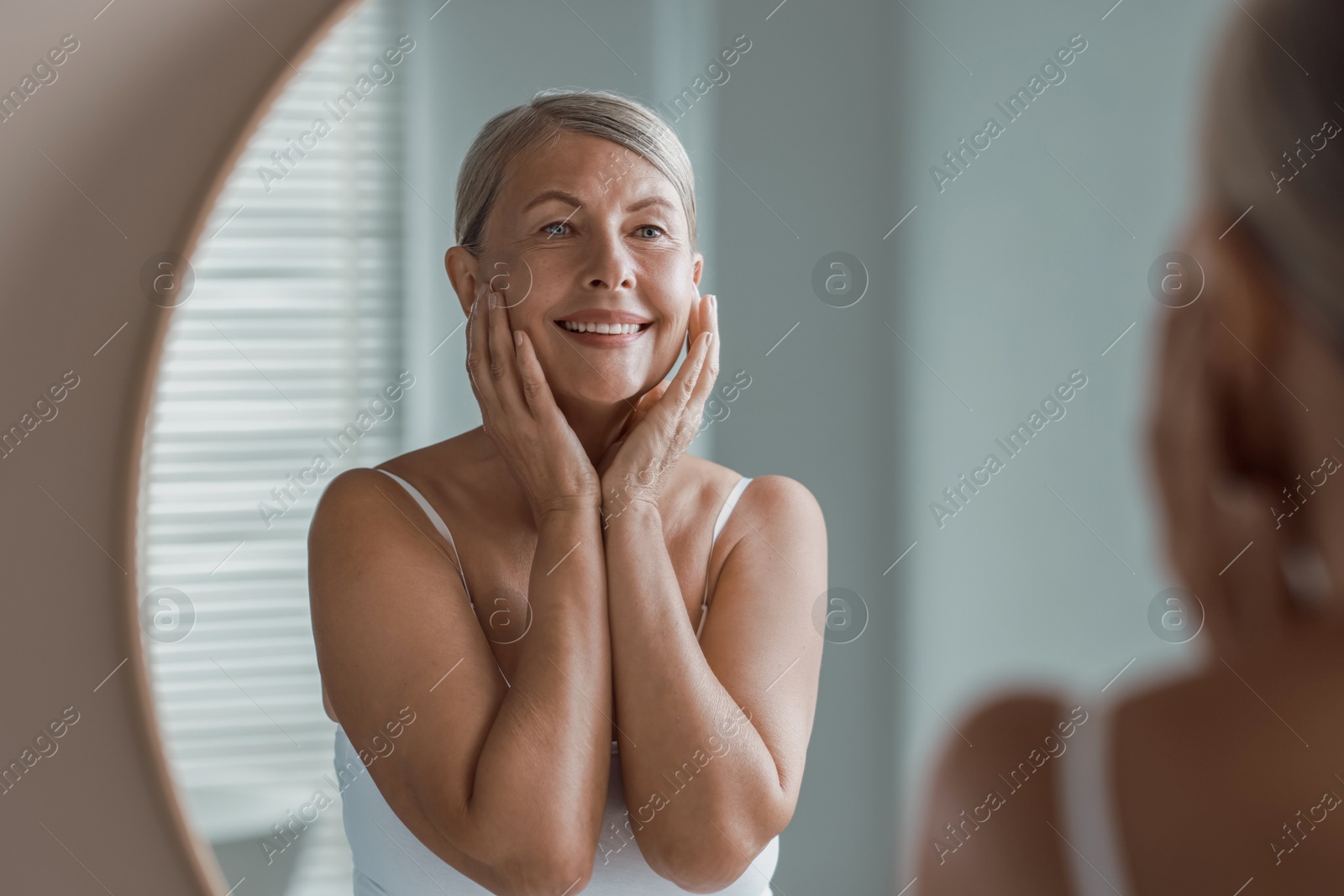 Photo of Face massage. Beautiful woman with healthy skin near mirror at home