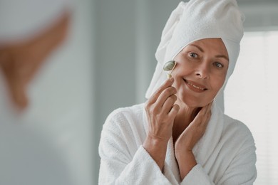 Photo of Beautiful woman doing facial massage with roller near mirror at home