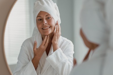 Beautiful woman doing facial massage near mirror at home