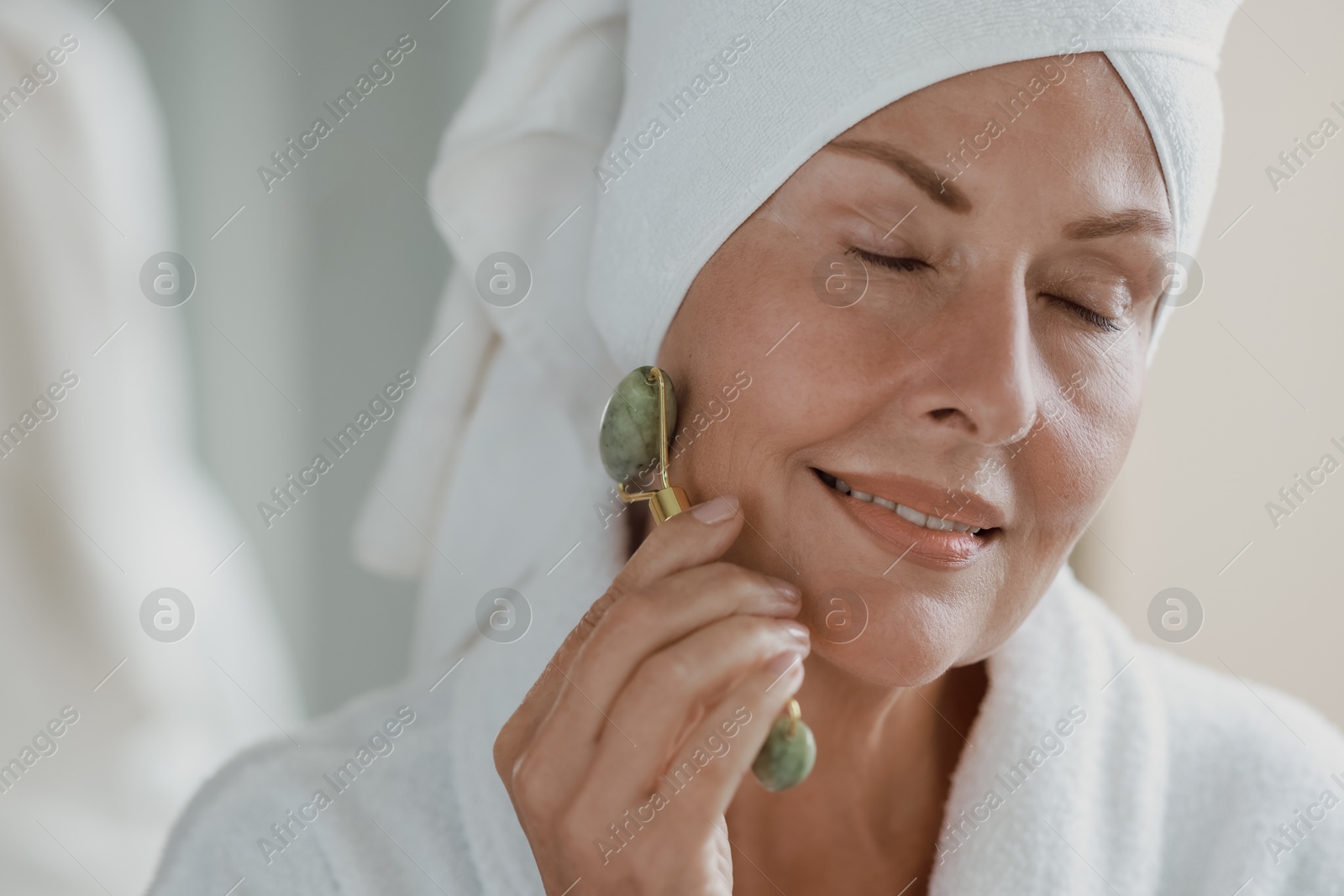 Photo of Beautiful woman doing facial massage with roller indoors, closeup