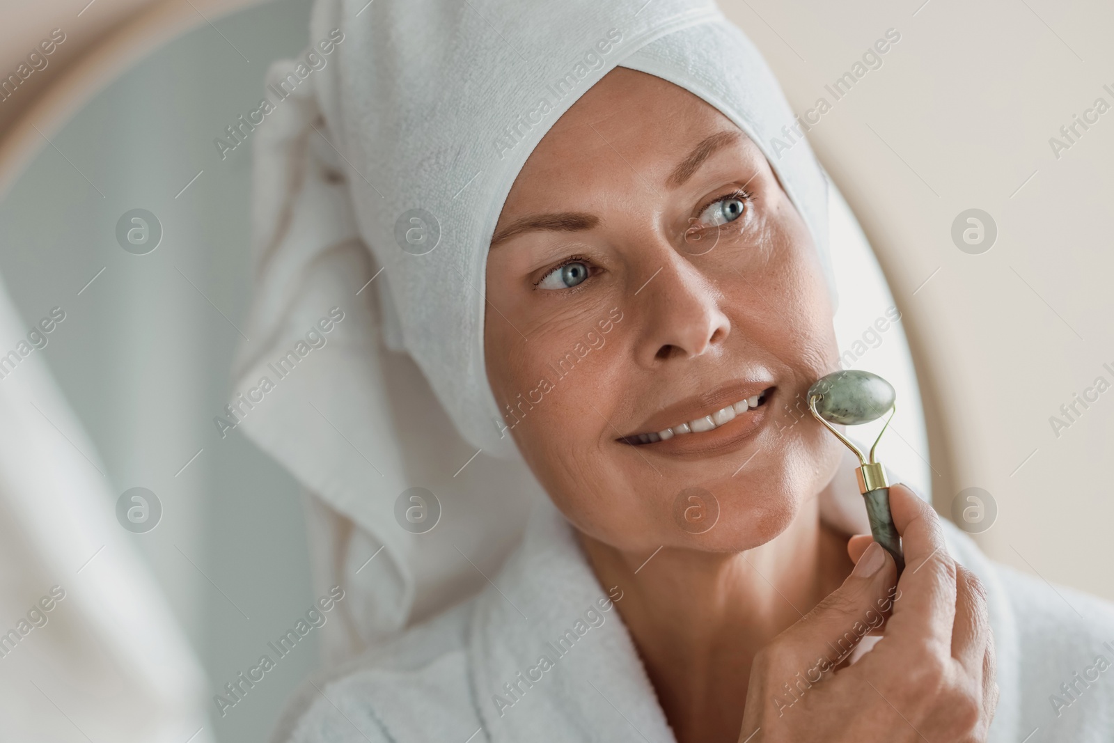 Photo of Beautiful woman doing facial massage with roller indoors, closeup