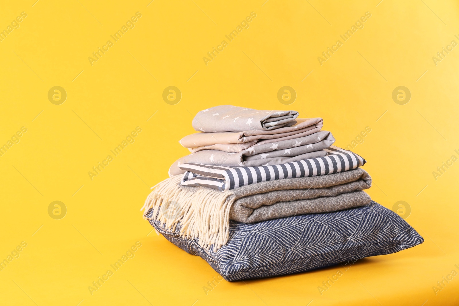 Photo of Stack of clean bed sheets and pillow on yellow background. Space for text