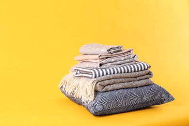 Stack of clean bed sheets and pillow on yellow background. Space for text