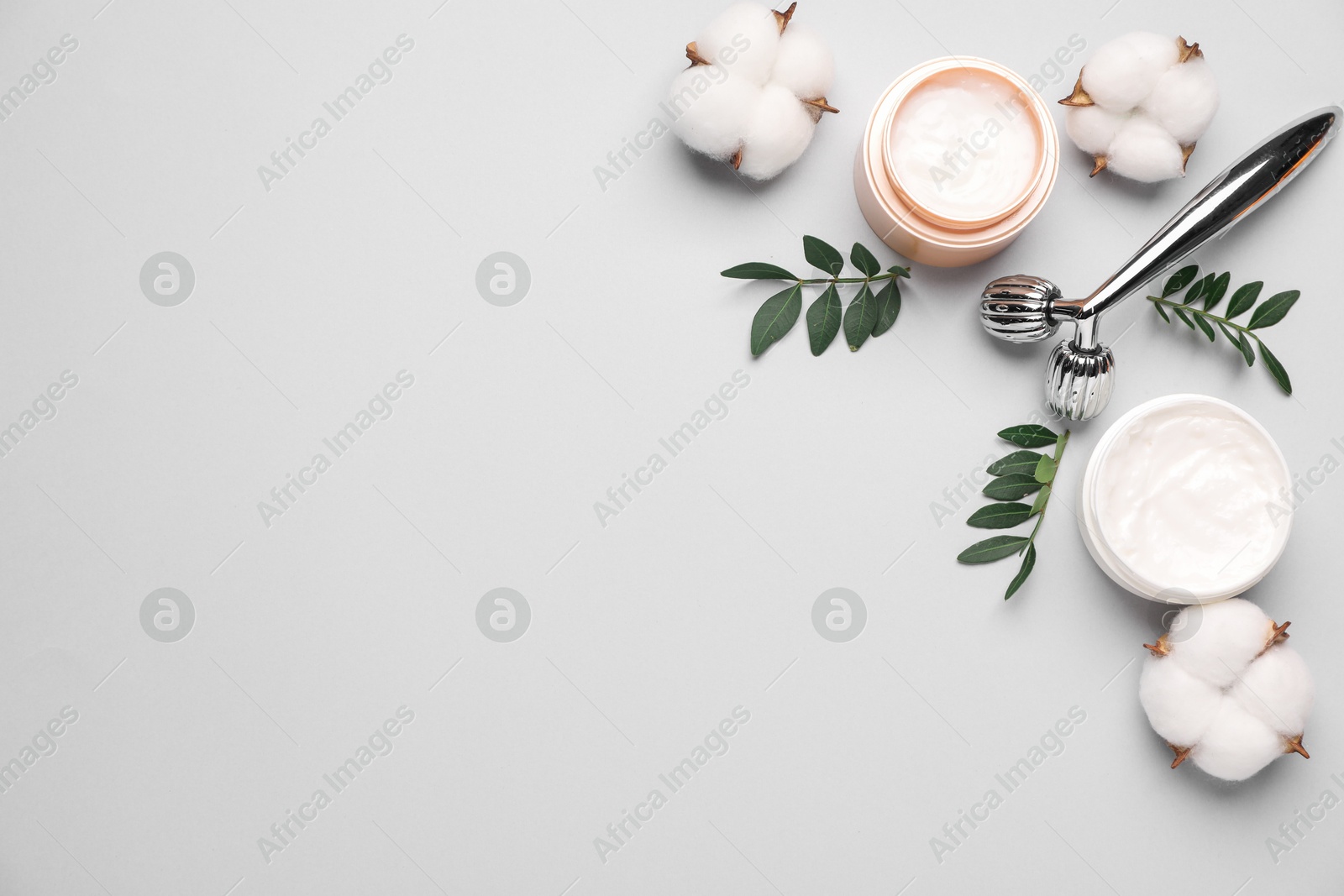 Photo of Different cosmetic products, green leaves and cotton flowers on light grey background, flat lay. Space for text