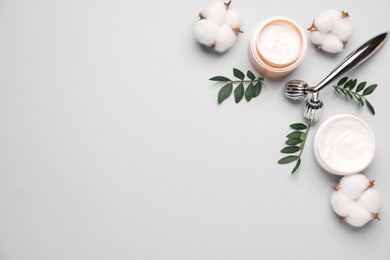 Photo of Different cosmetic products, green leaves and cotton flowers on light grey background, flat lay. Space for text