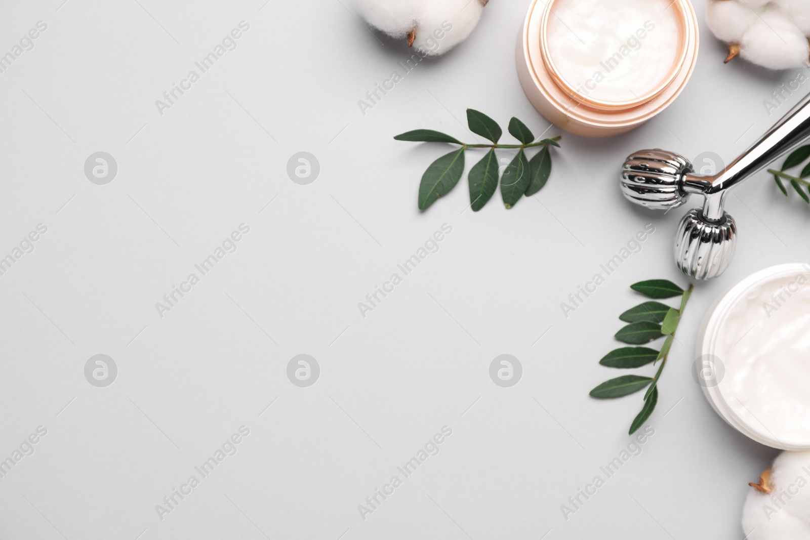 Photo of Different cosmetic products, green leaves and cotton flowers on light grey background, flat lay. Space for text