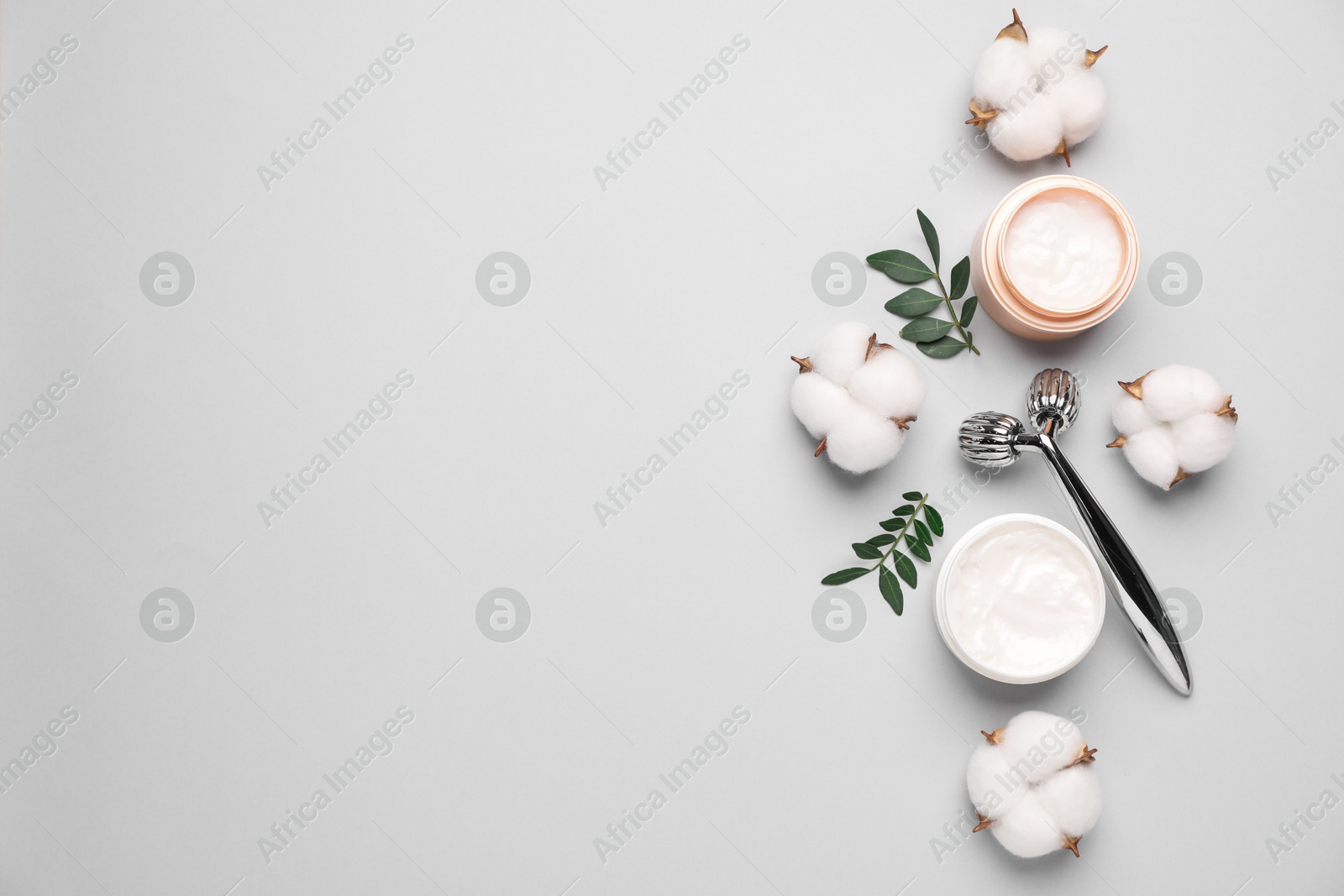 Photo of Different cosmetic products, green leaves and cotton flowers on light grey background, flat lay. Space for text