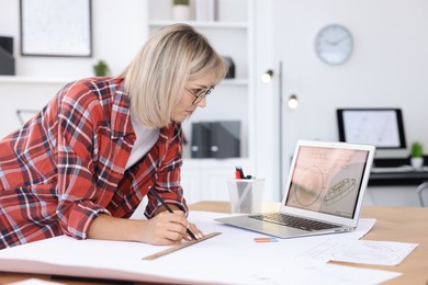 Architect making engineering drawing at wooden table in office