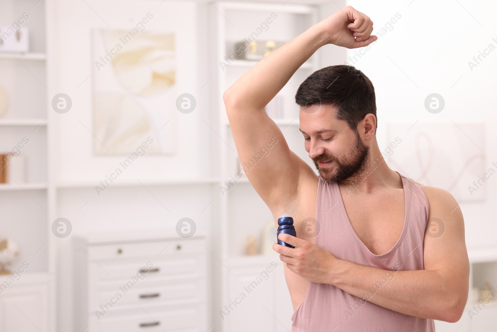 Photo of Man applying roll-on deodorant at home. Space for text