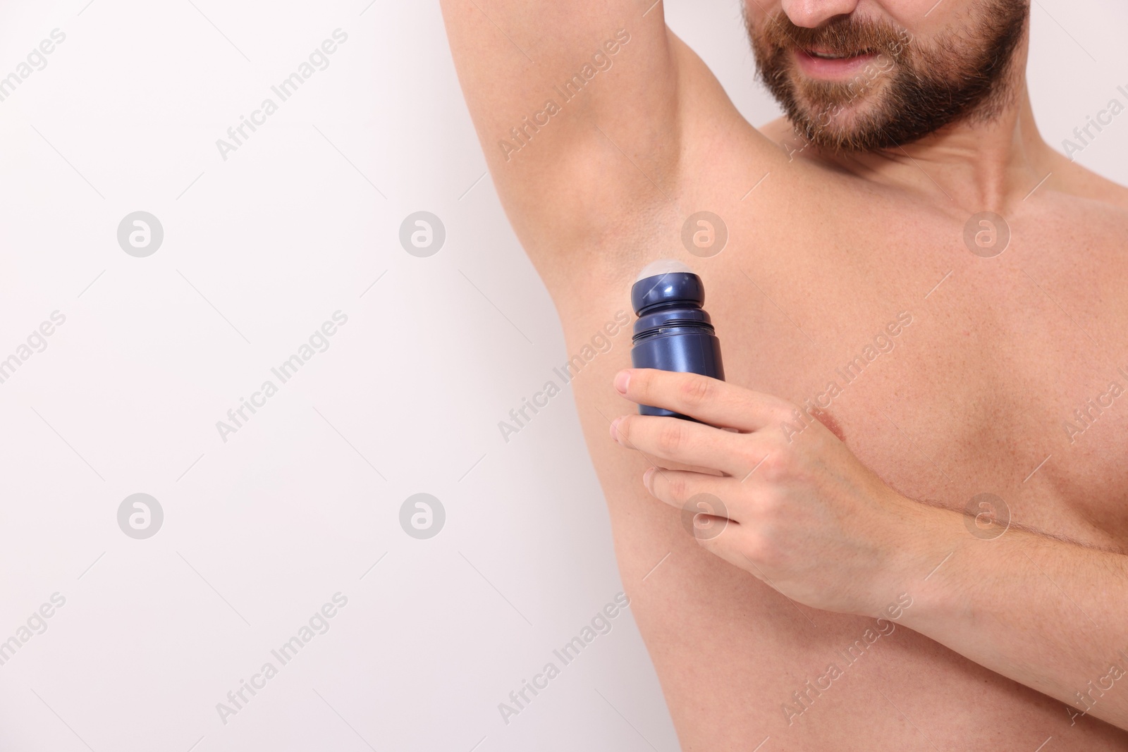 Photo of Man applying roll-on deodorant on white background, closeup. Space for text