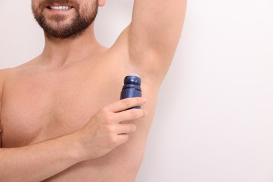 Smiling man applying roll-on deodorant on white background, closeup. Space for text